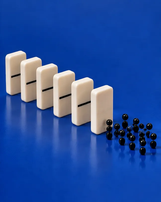 Six white dominoes stand in a neat row on a blue floor, and the last one has spilled all of its black dots out onto the ground.